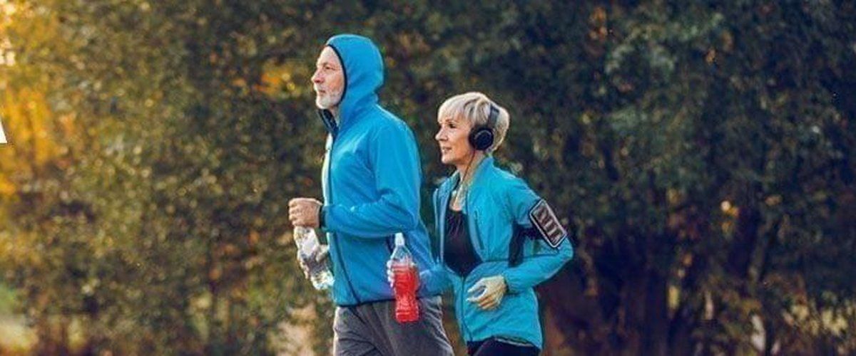 An active older couple jogging through a park